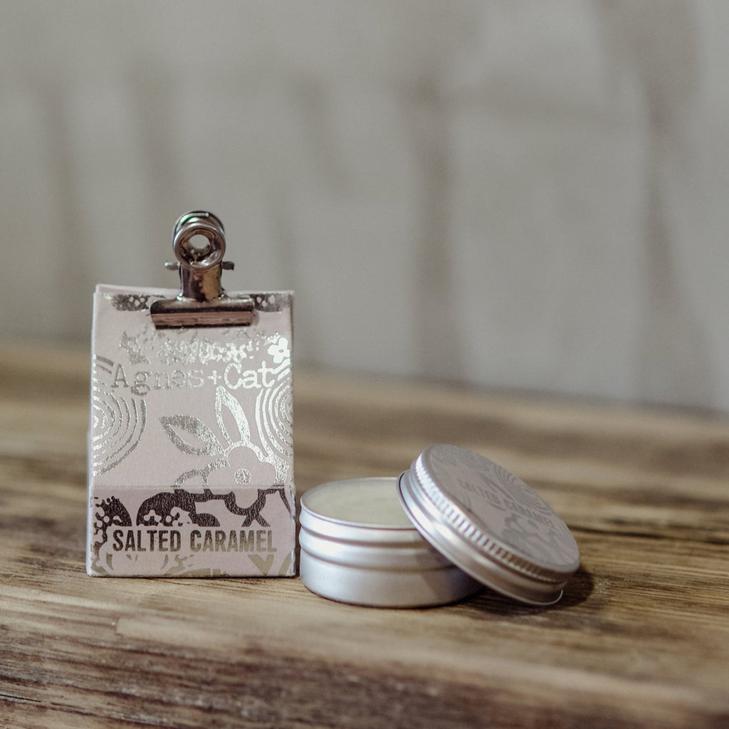 Small tin of salted caramel lip balm with a decorative gift box. image on a wooden surface